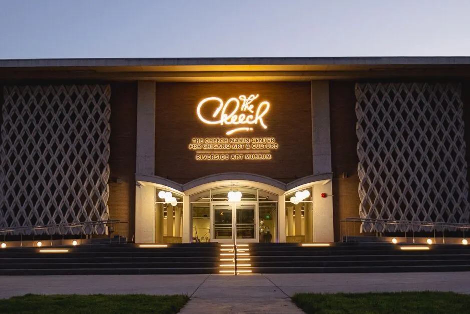 Exterior view of The Cheech Marin Center for Chicano Art and Culture at Riverside Art Museum at dusk with illuminated signage and modern architectural design.