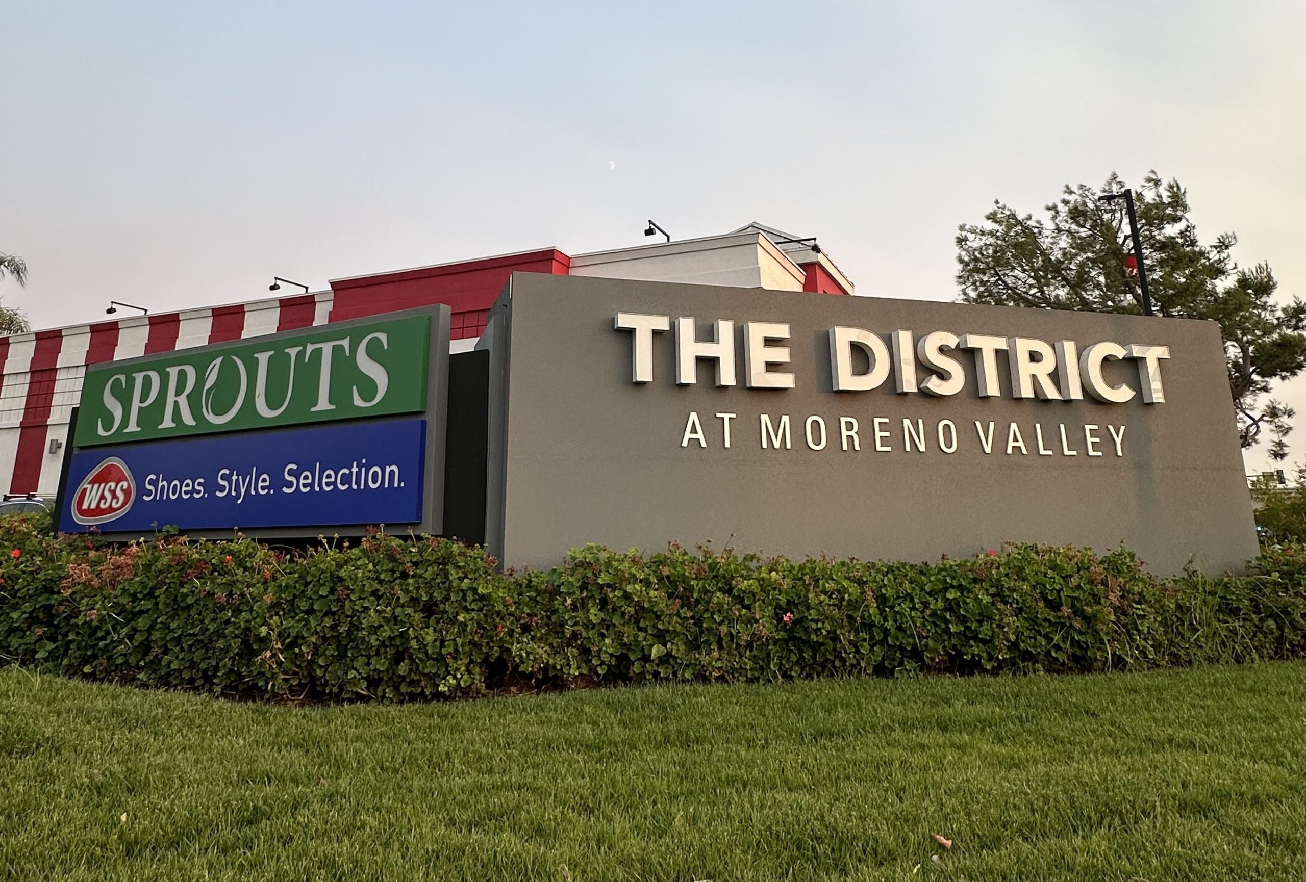 Signs for Sprouts and The District at Moreno Valley shopping center, amid greenery and a manicured lawn.