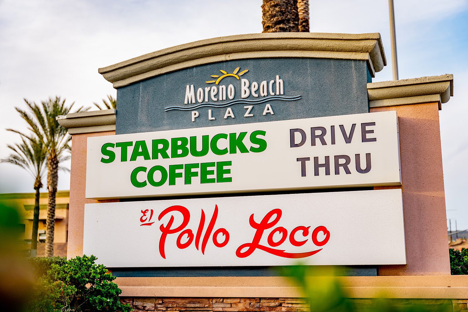 A sign at Moreno Beach Plaza displaying Starbucks Coffee Drive Thru on top and El Pollo Loco below.