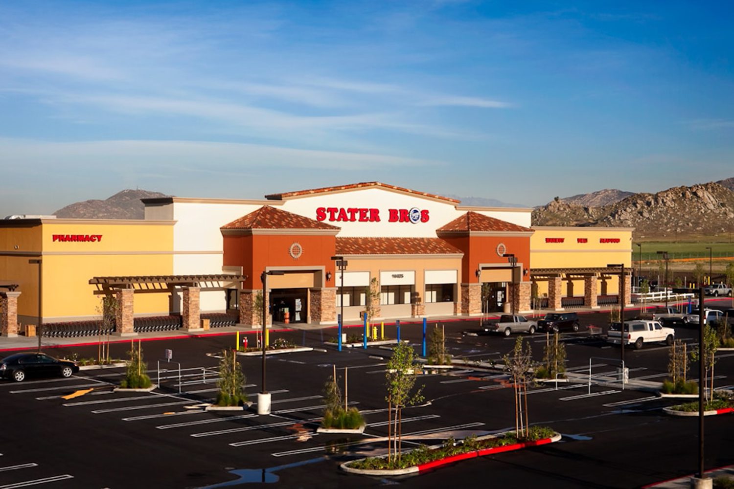 A Stater Bros. grocery store with an adjacent parking lot is seen under a clear blue sky, with mountains visible in the background.