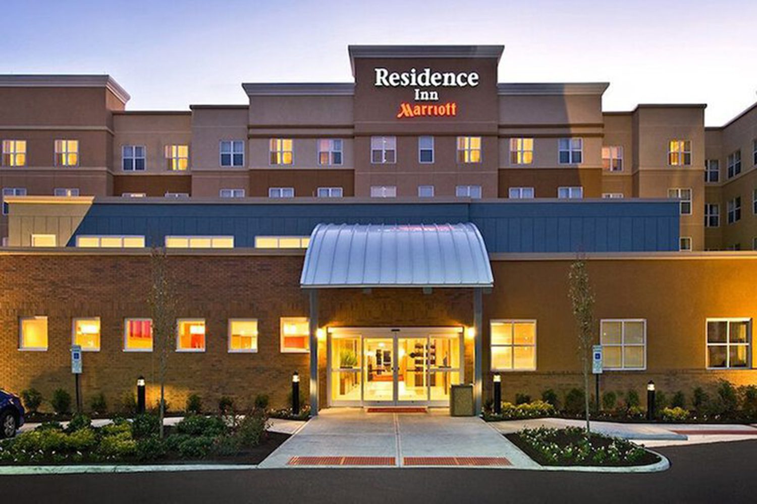 A multi-story hotel building with "Residence Inn Marriott" signage above the entrance, featuring large windows and a well-lit exterior.