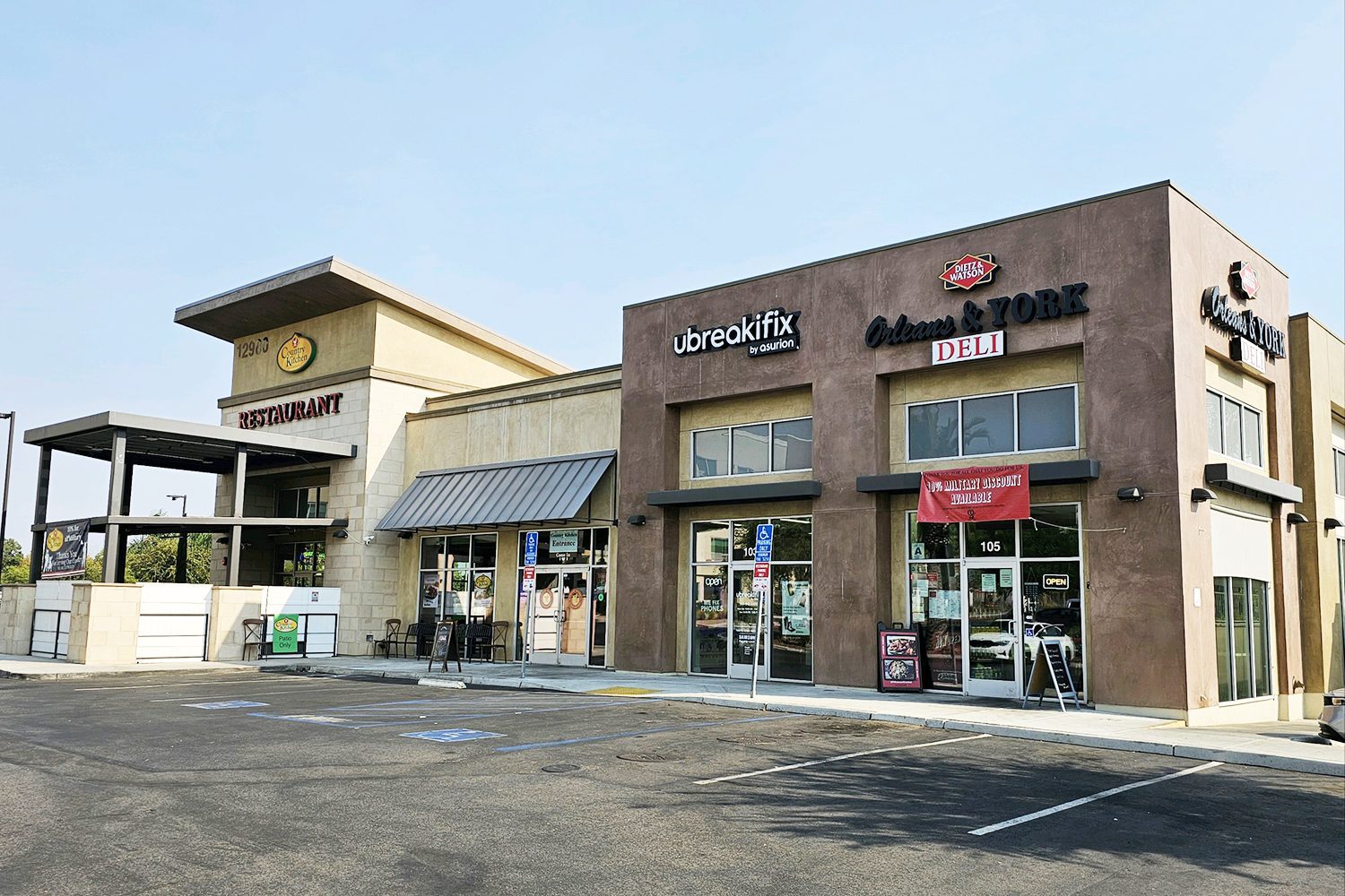 A strip mall with a restaurant, a uBreakiFix electronics repair store, and a delicatessen. The parking lot in front has several open spaces.