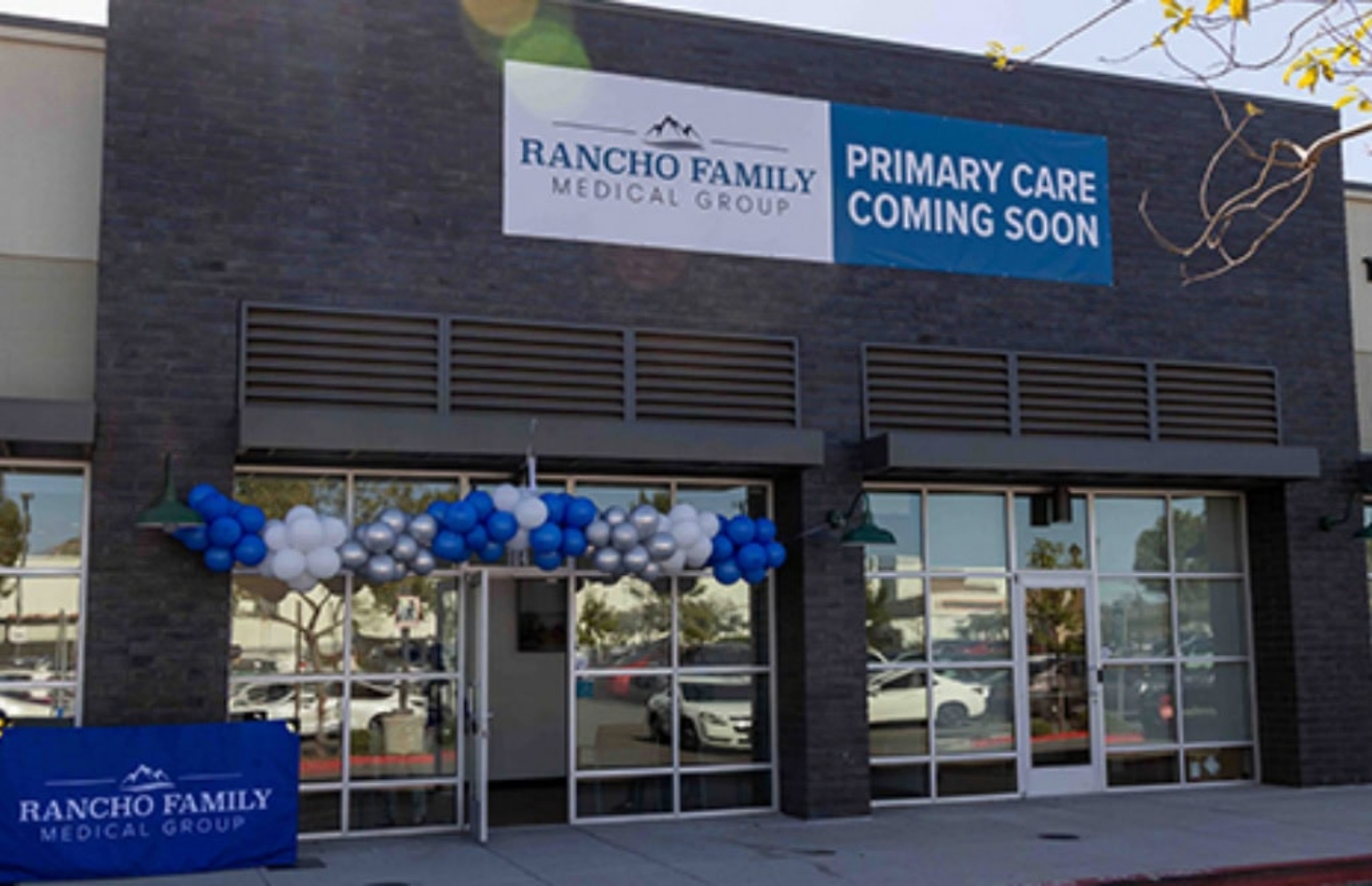 A new Rancho Family Medical Group clinic with a banner announcing primary care services coming soon, decorated with blue and white balloons outside the building.